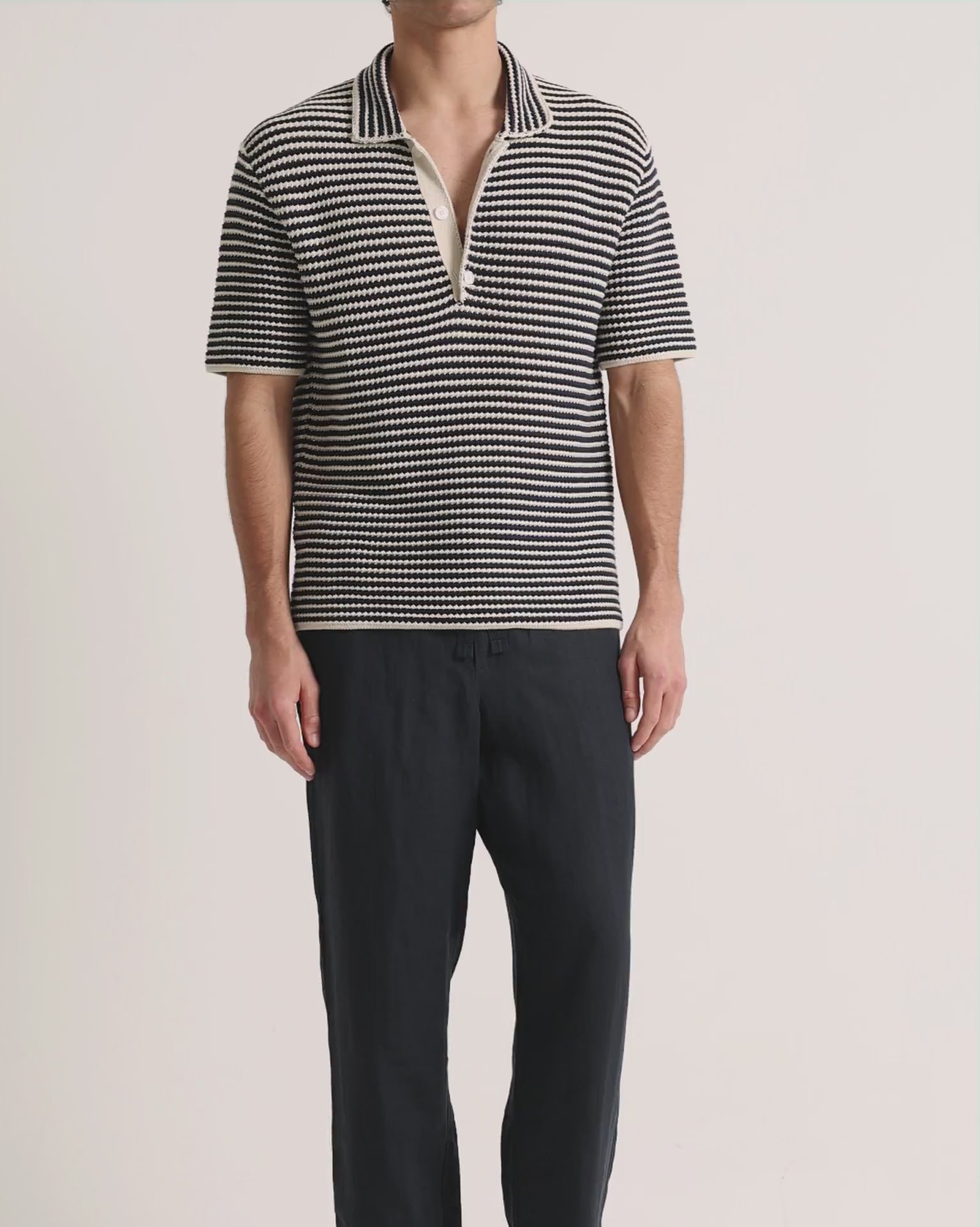 Man wearing navy crochet polo shirt with navy trousers on a plain background