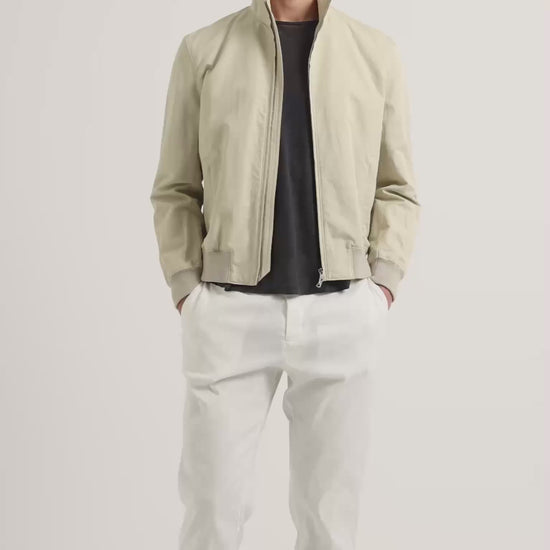 Man wearing light beige zip up jacket with dark grey t-shirt and white trousers