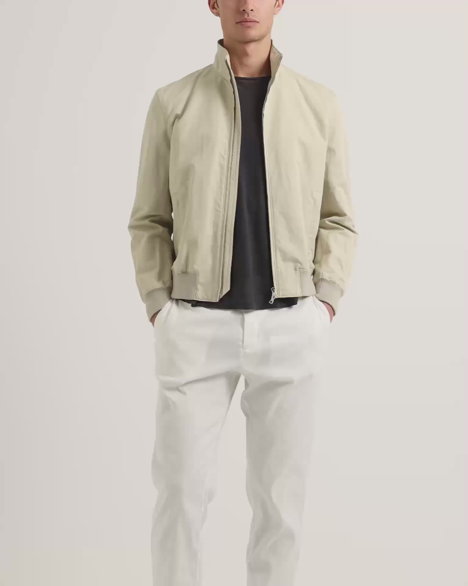 Man wearing light beige zip up jacket with dark grey t-shirt and white trousers