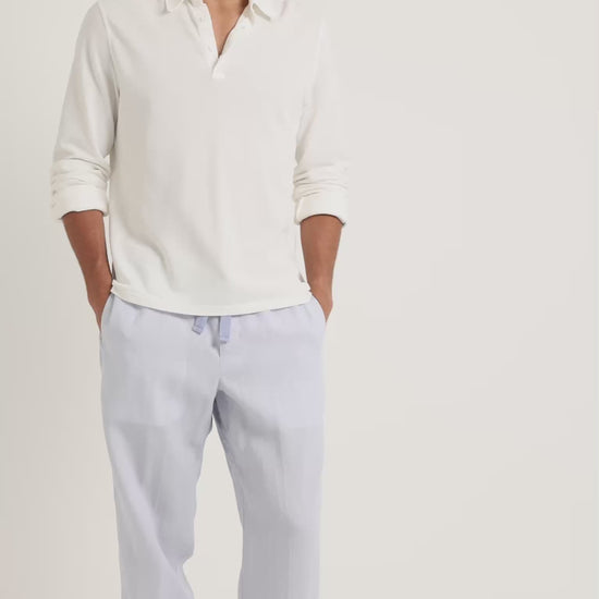 Man wearing long-sleeve white shirt with blue trousers on a plain background