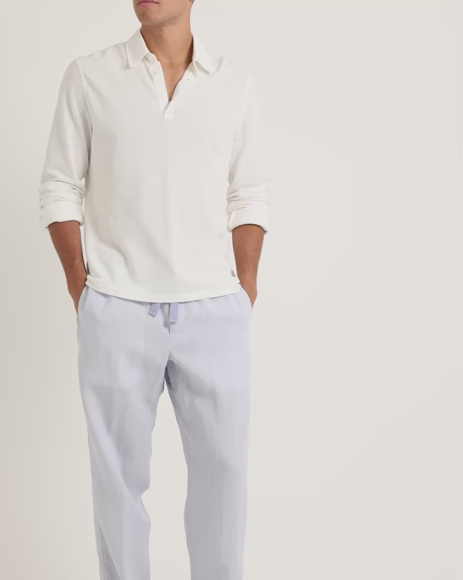 Man wearing long-sleeve white shirt with blue trousers on a plain background