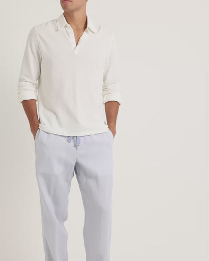 Man wearing long-sleeve white shirt with blue trousers on a plain background