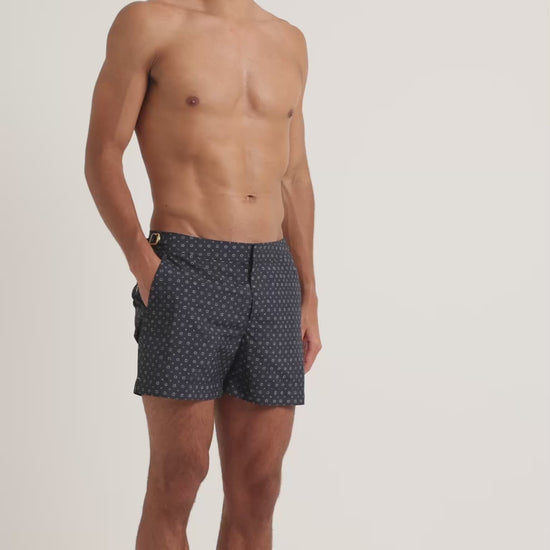 Man wearing navy geometric print swim shorts on a plain background