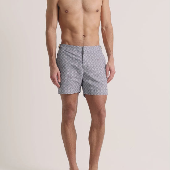 Man wearing light grey printed swim shorts on a plain background