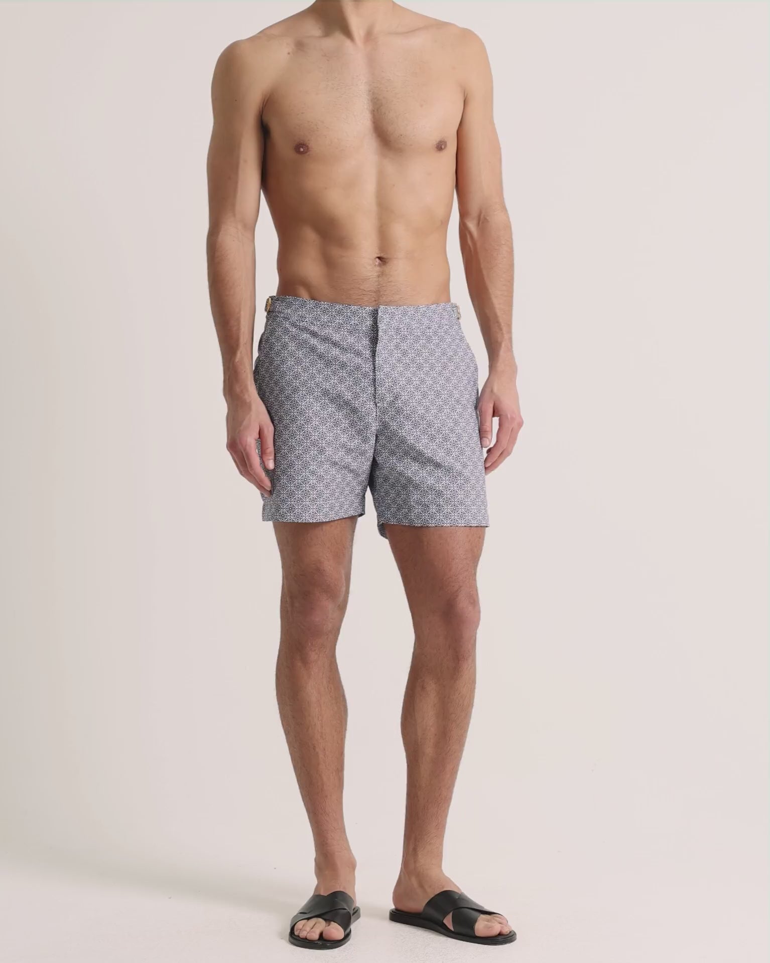 Man wearing light grey printed swim shorts on a plain background
