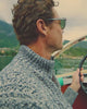 Man wearing grey and white quarter zip knitted jumper whilst on a boat on a lake