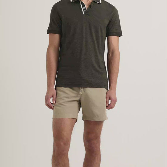Man wearing dark green polo shirt with white tipping on collar with beige shorts