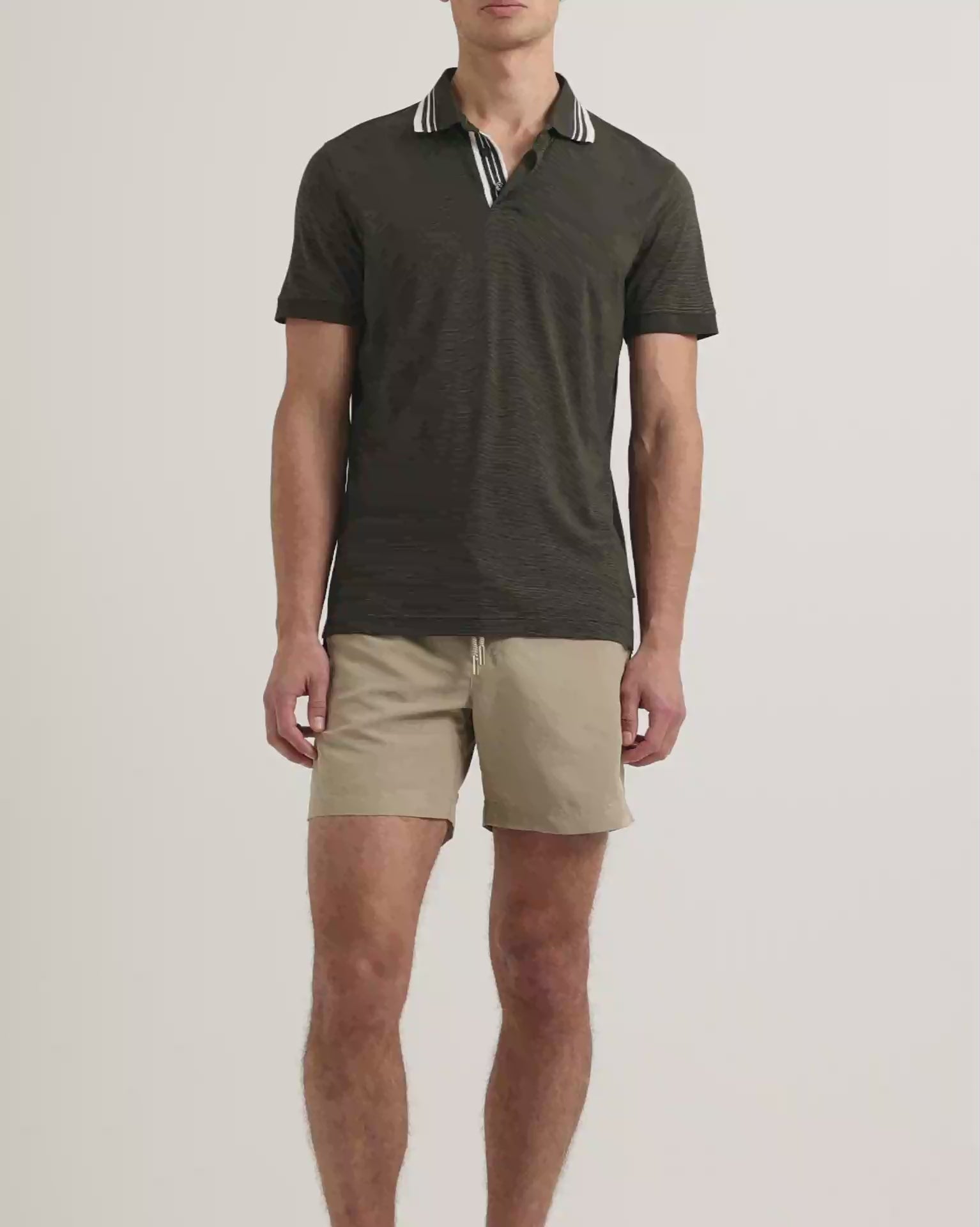 Man wearing dark green polo shirt with white tipping on collar with beige shorts