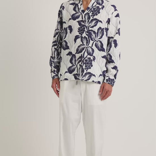 Man wearing floral print navy and white shirt with white trousers on a white background