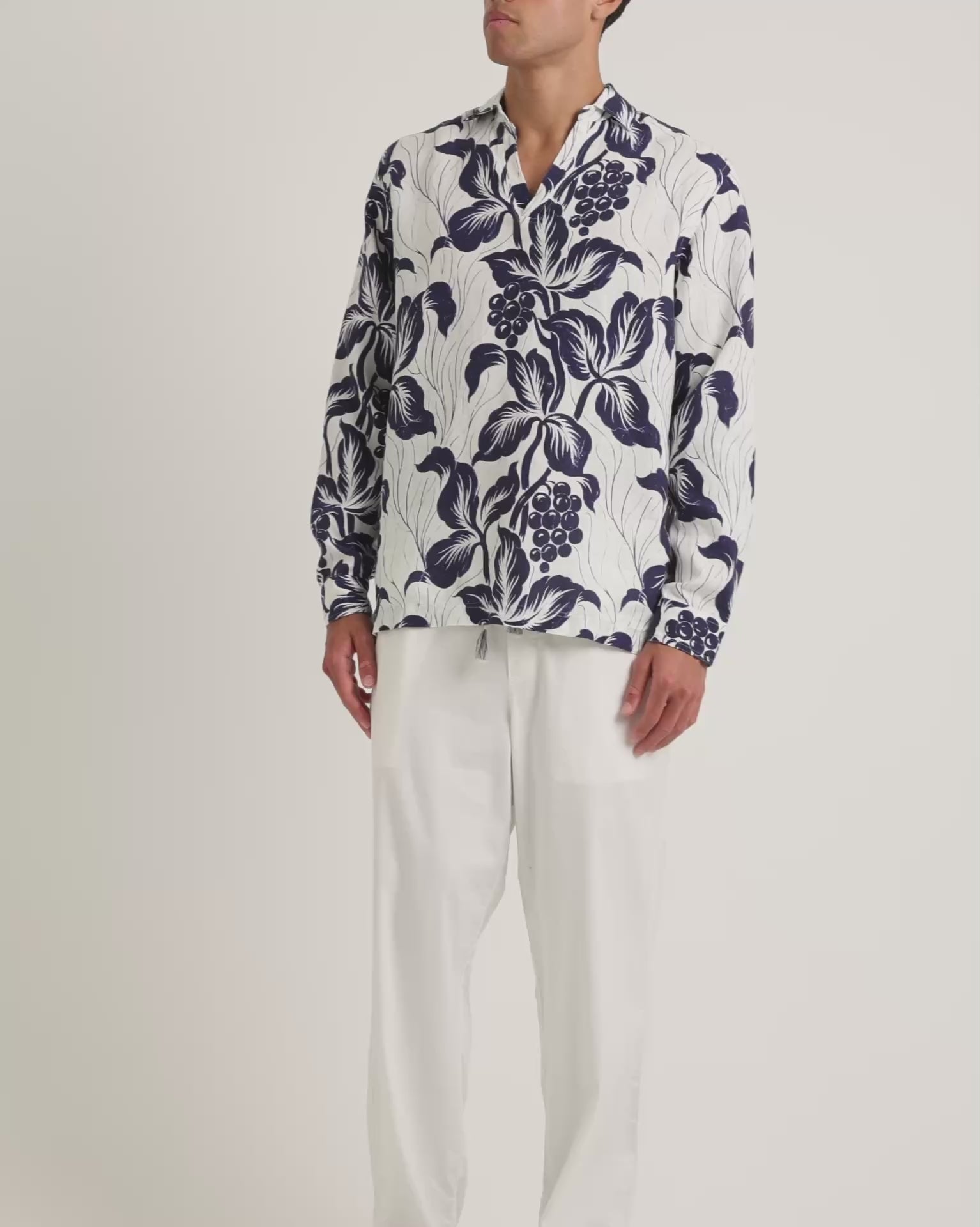 Man wearing floral print navy and white shirt with white trousers on a white background