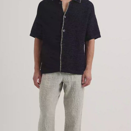 Man wearing crochet stitch shirt in navy with white detailing, with beige linen trousers