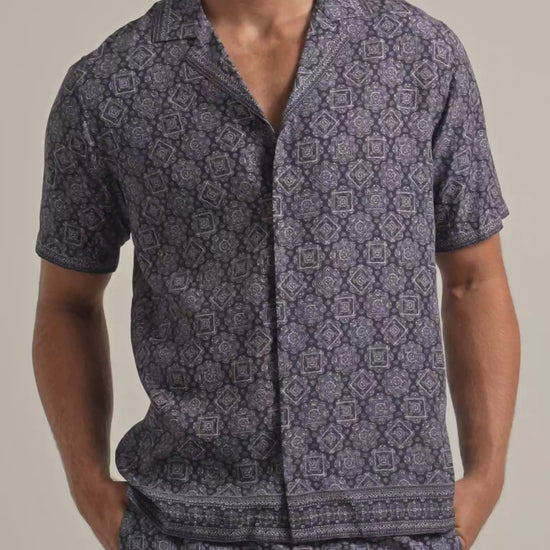 Man wearing navy and white geometric print shirt with matching swim shorts against a plain background