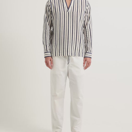 Man wearing long sleeve striped shirt in navy and white with white drawstring trousers