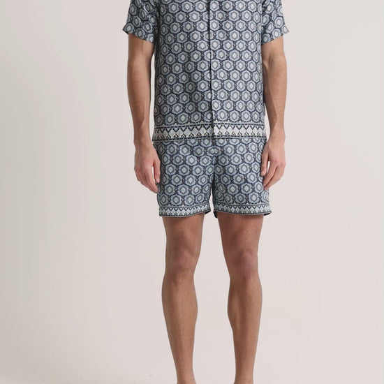 Man wearing blue printed shirt and swim shorts on a plain background