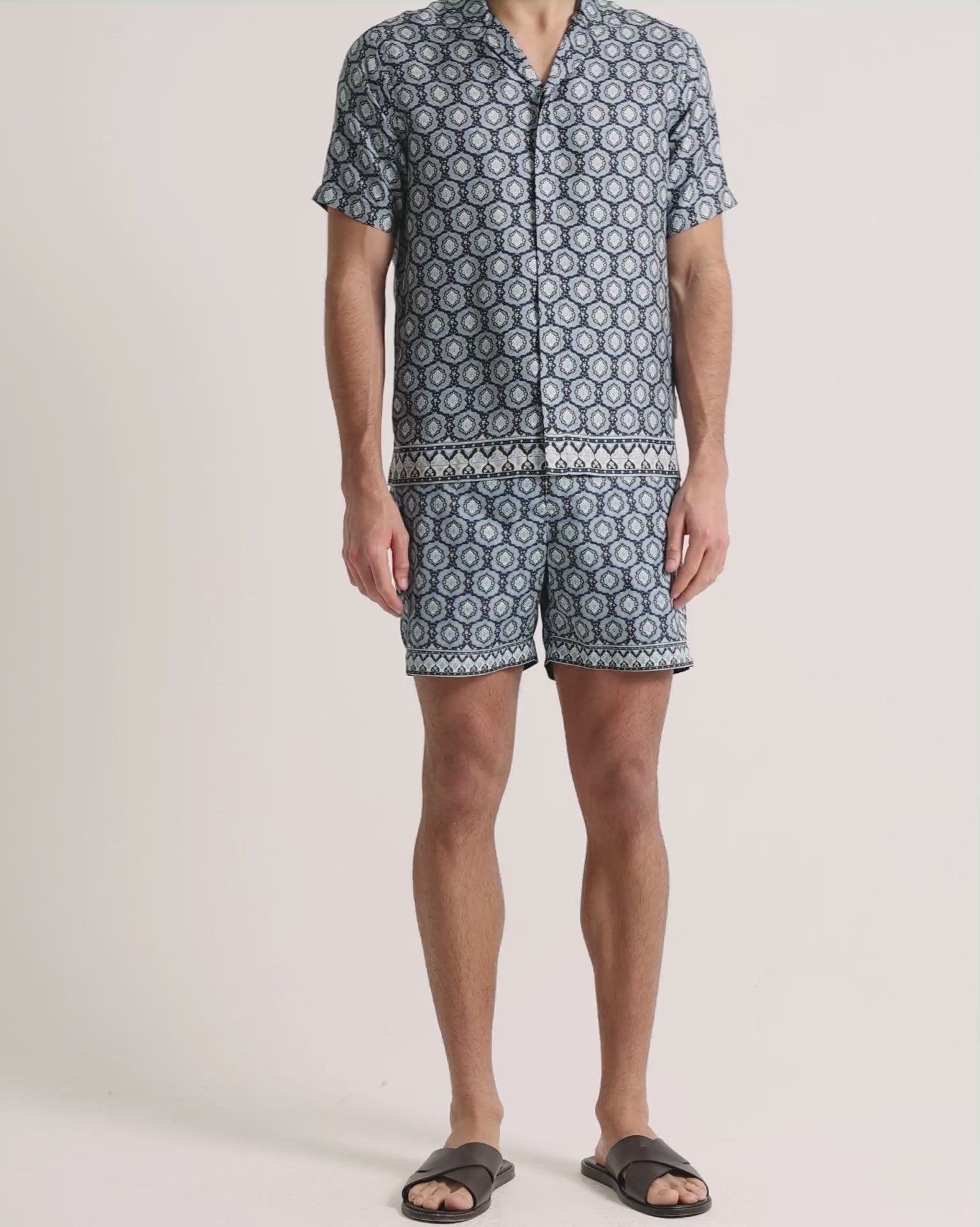 Man wearing blue printed shirt and swim shorts on a plain background