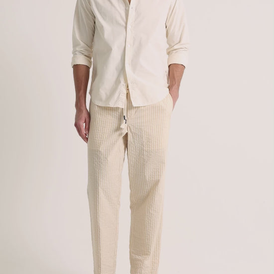 Man wearing beige shirt with beige striped trousers on a plain background