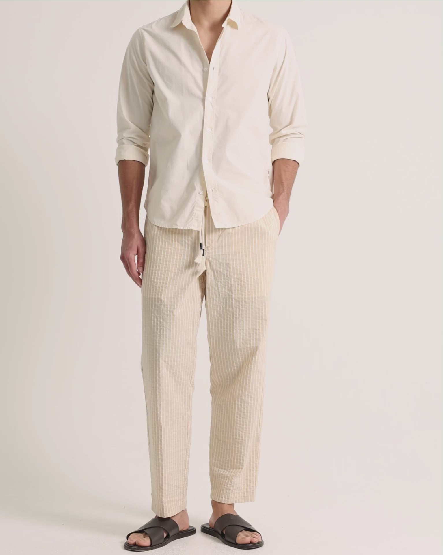 Man wearing beige shirt with beige striped trousers on a plain background