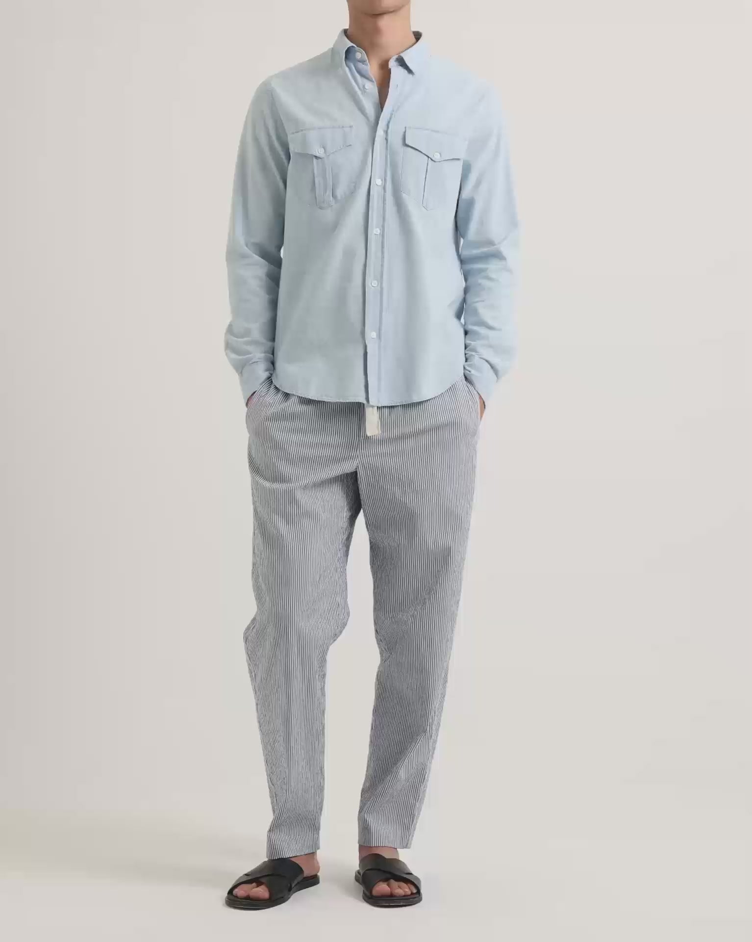 Man wearing light blue shirt with chest pockets and blue seersucker linen trousers with drawstring waist