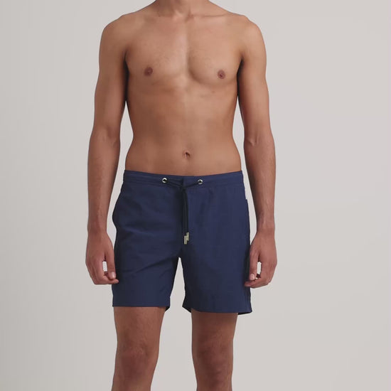 Man wearing navy drawstring swim shorts on a plain background 