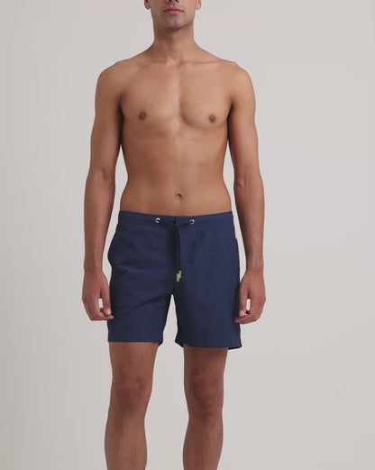 Man wearing navy drawstring swim shorts on a plain background 