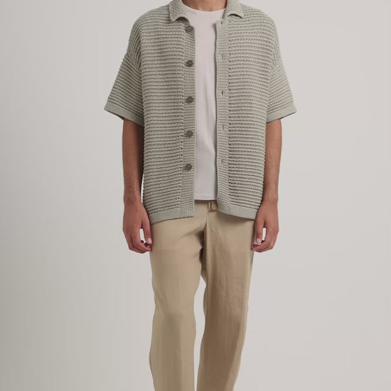 Man wearing green knitted shirt with beige trousers and trousers on a white background