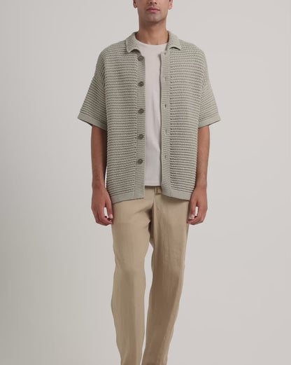 Man wearing green knitted shirt with beige trousers and trousers on a white background