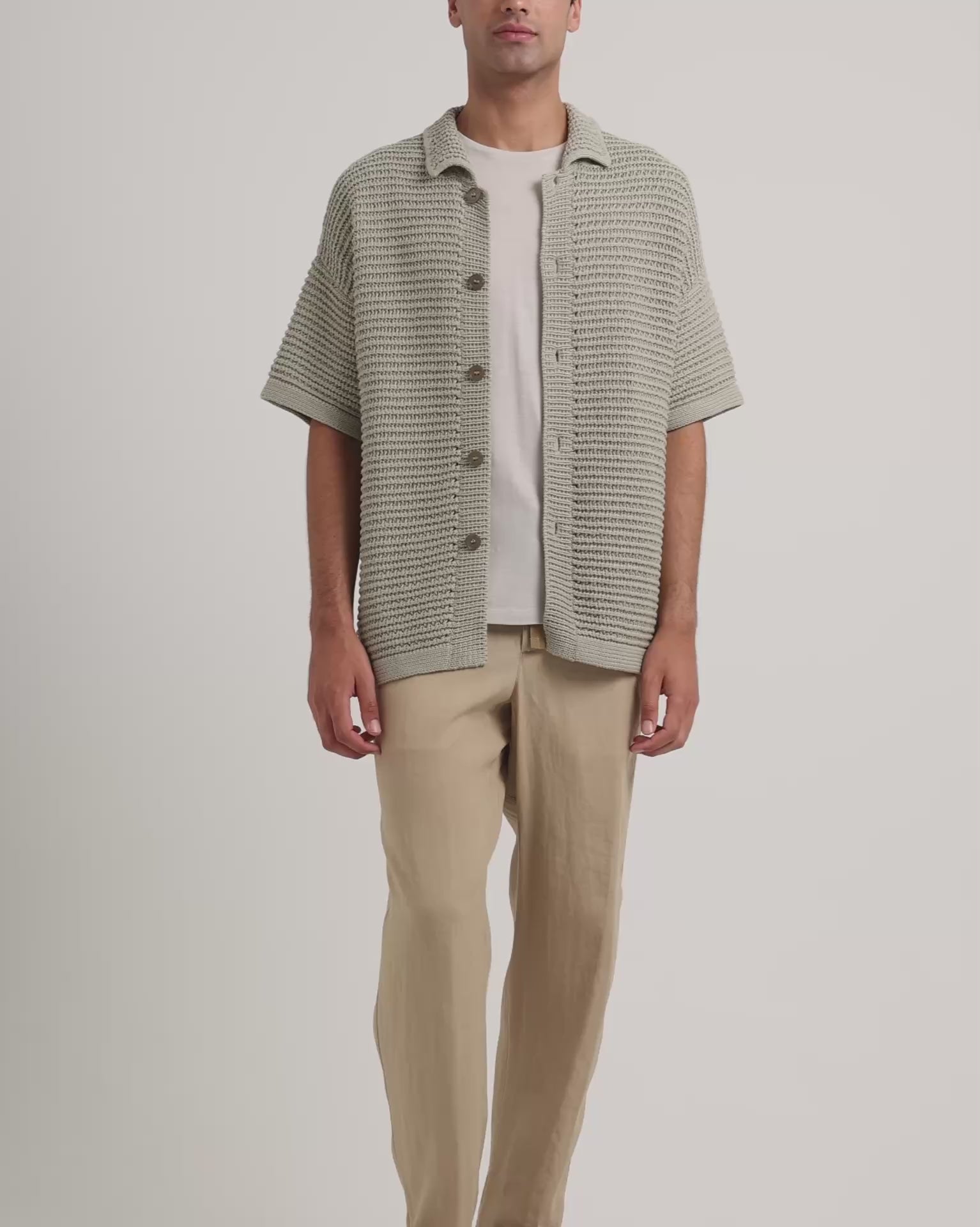 Man wearing green knitted shirt with beige trousers and trousers on a white background