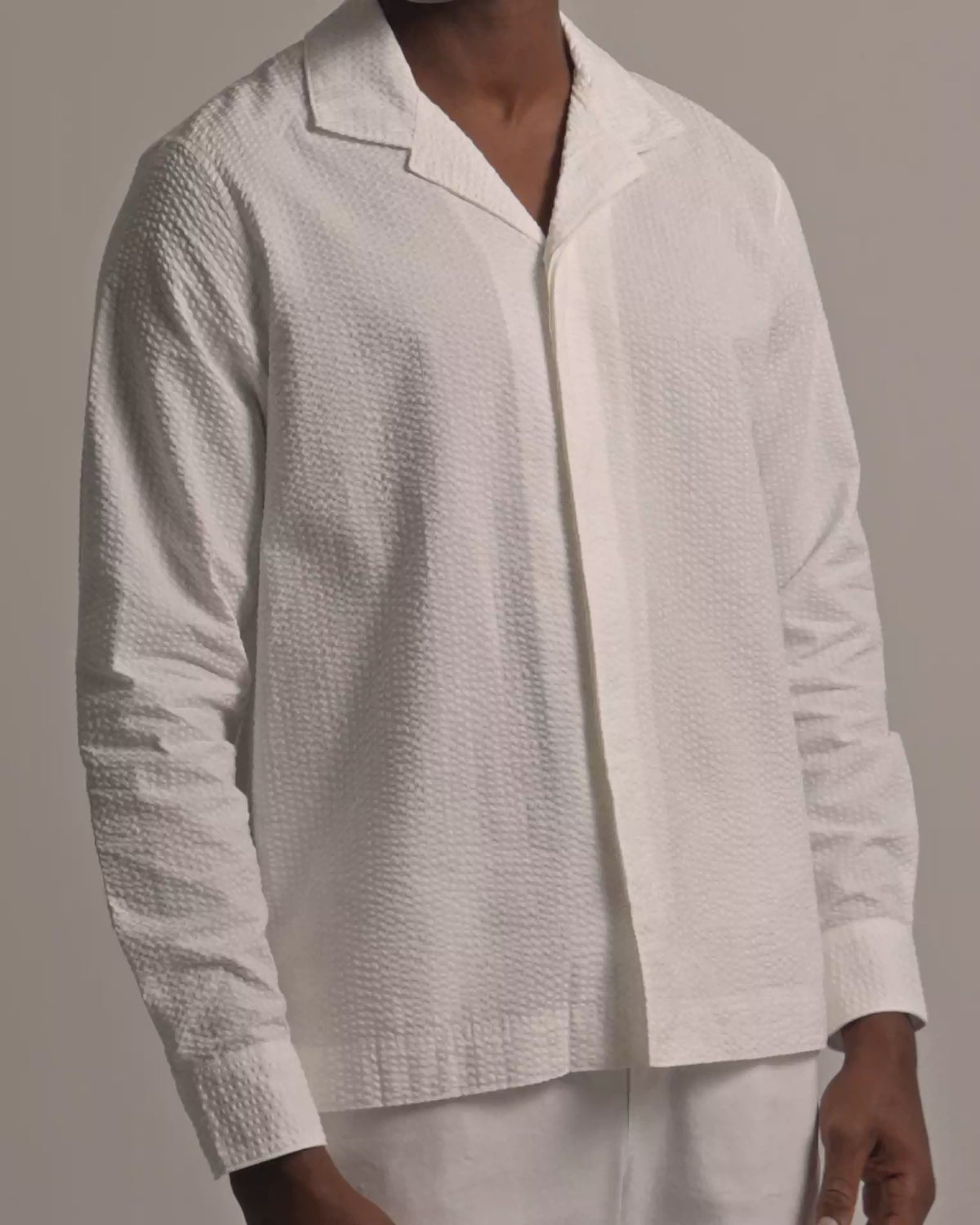 Man wearing white seersucker shirt with white trousers against a plain background