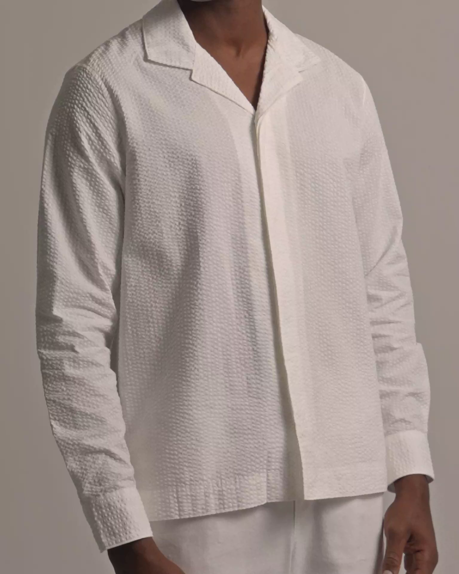 Man wearing white seersucker shirt with white trousers against a plain background