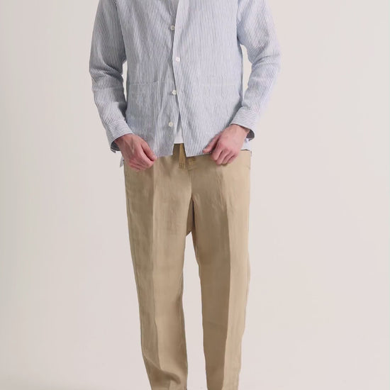 Man wearing striped overshirt with beige trousers on a plain background