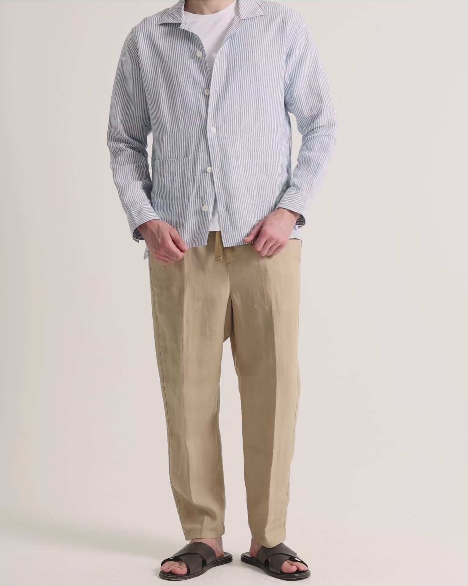 Man wearing striped overshirt with beige trousers on a plain background