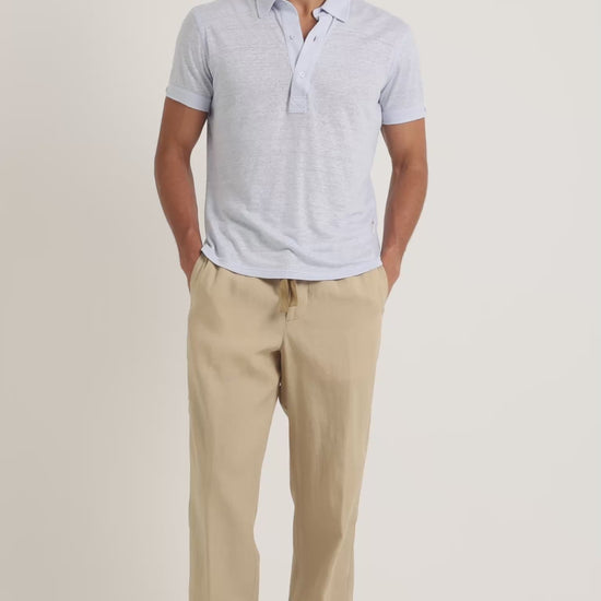 Man wearing light blue polo shirt with beige trousers on a plain background