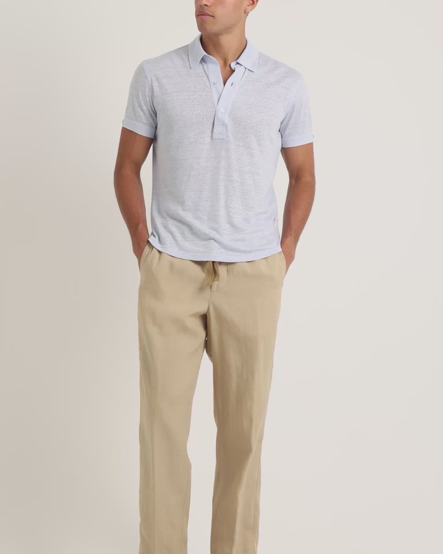 Man wearing light blue polo shirt with beige trousers on a plain background