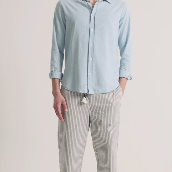 Man wearing blue shirt with grey striped trousers on a plain background