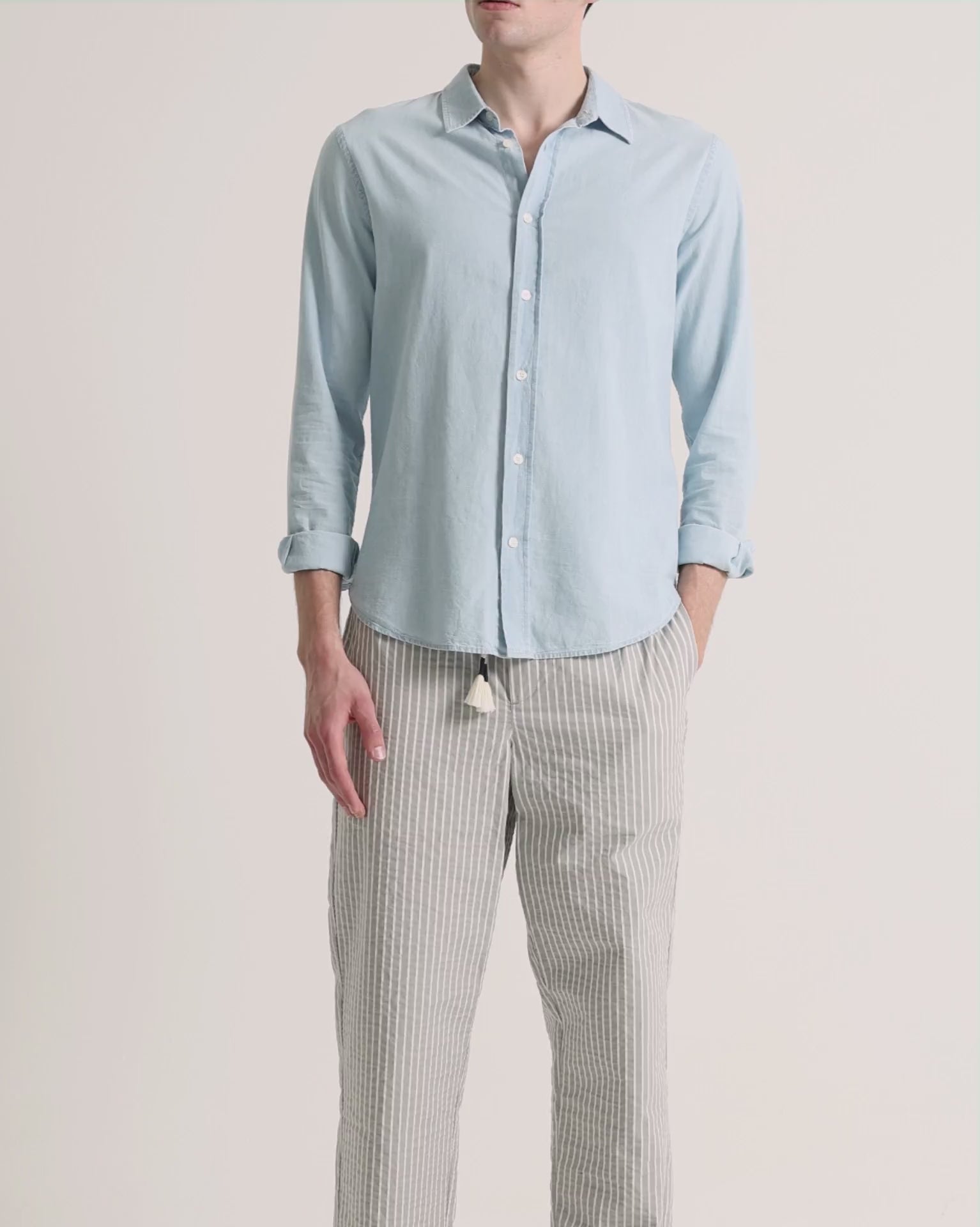 Man wearing blue shirt with grey striped trousers on a plain background