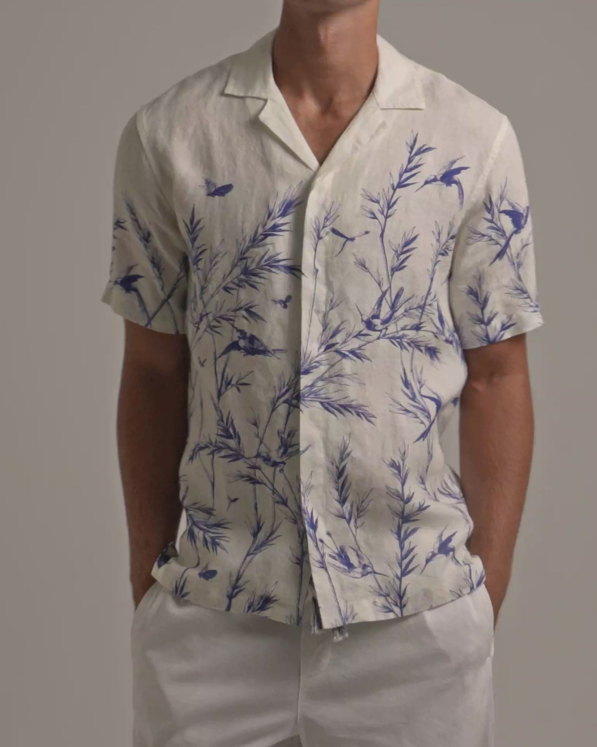 Man wearing white linen shirt with blue botanical print and white trousers on a plain background