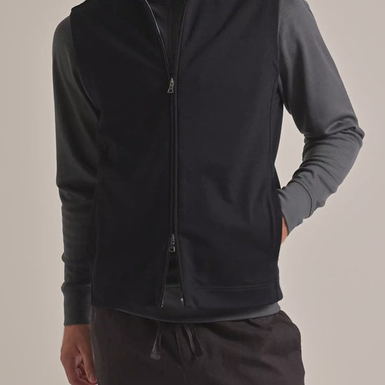 Man wearing lightweight gilet with grey quarter-zip sweatshirt underneath and dark brown trousers on a plain background
