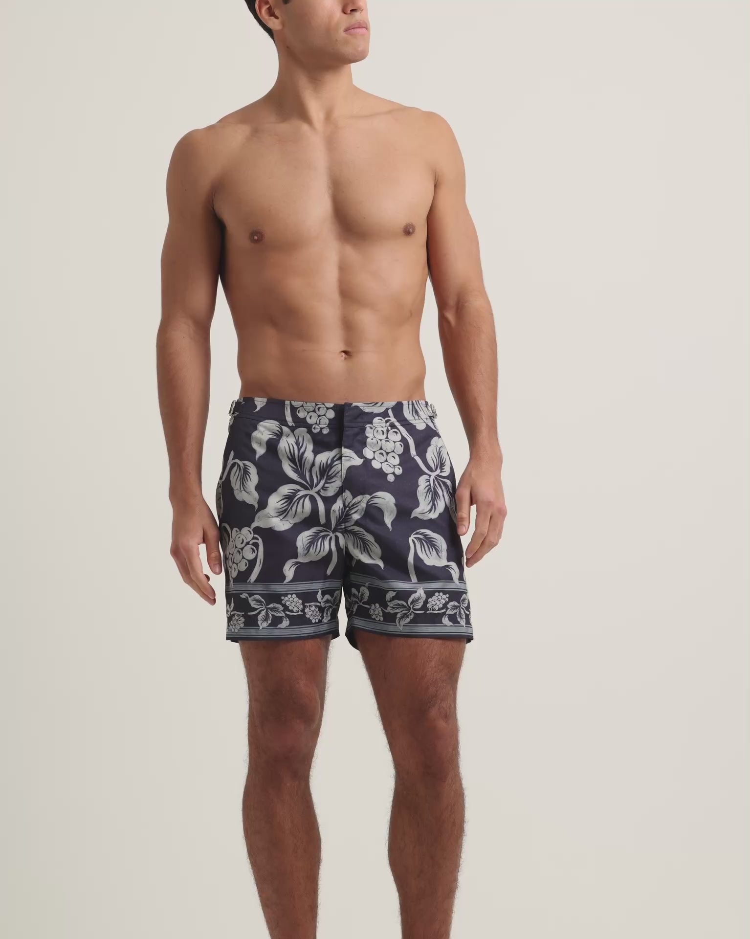 Man wearing navy floral swim shorts on a plain background