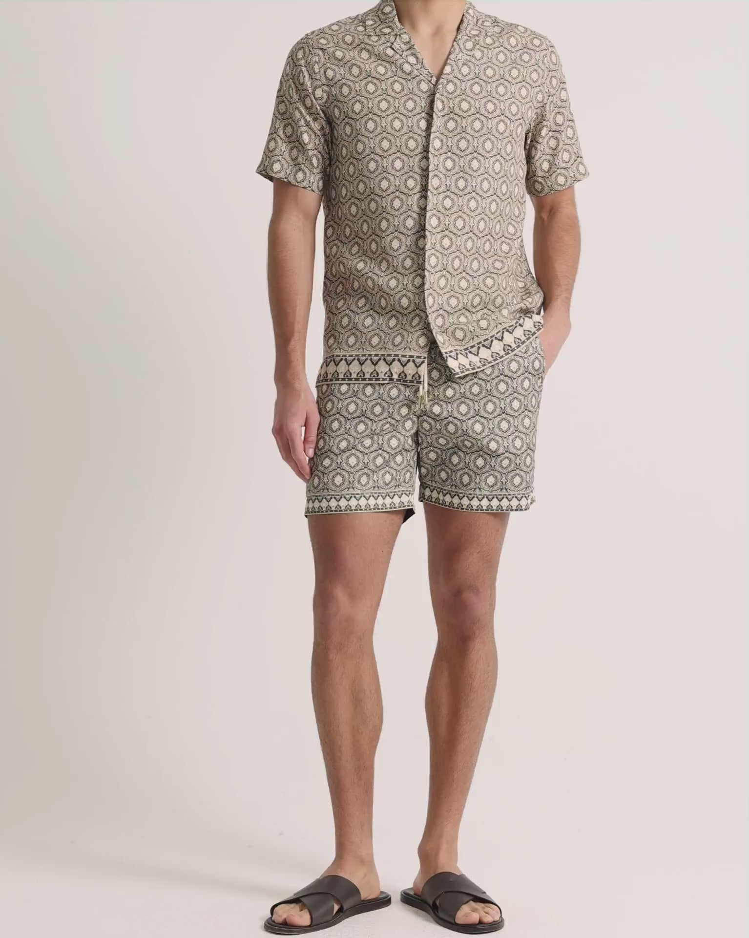 Man wearing beige printed shirt with shorts on a plain background