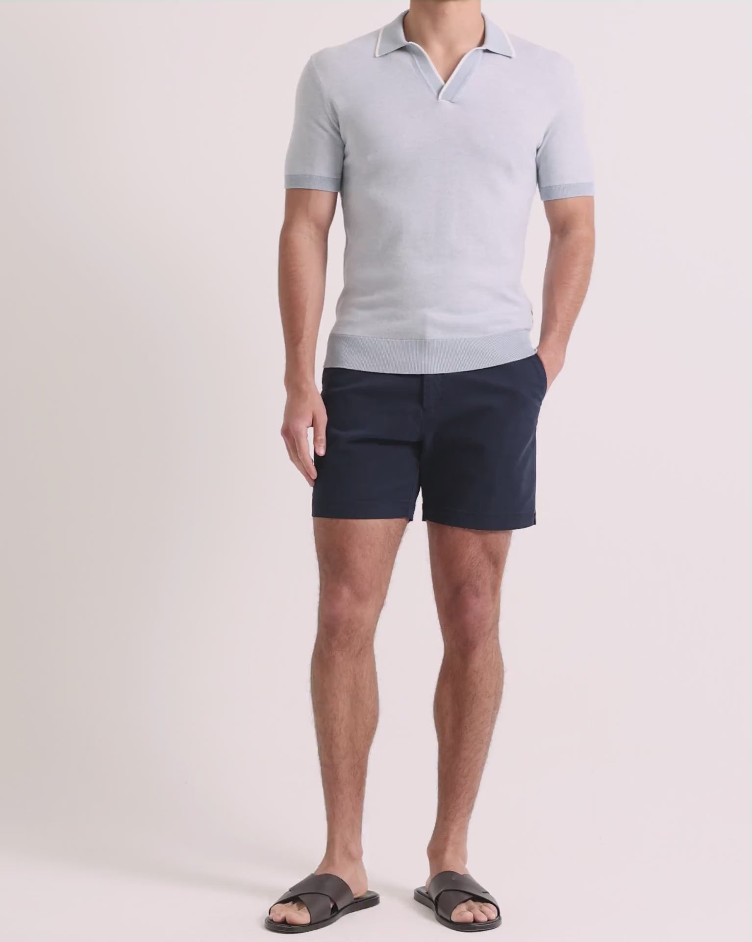 Man wearing blue knitted polo shirt with navy shorts on a plain background