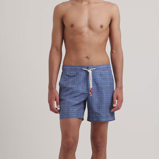 Man wearing geometric print blue drawstring swim shorts on a plain background
