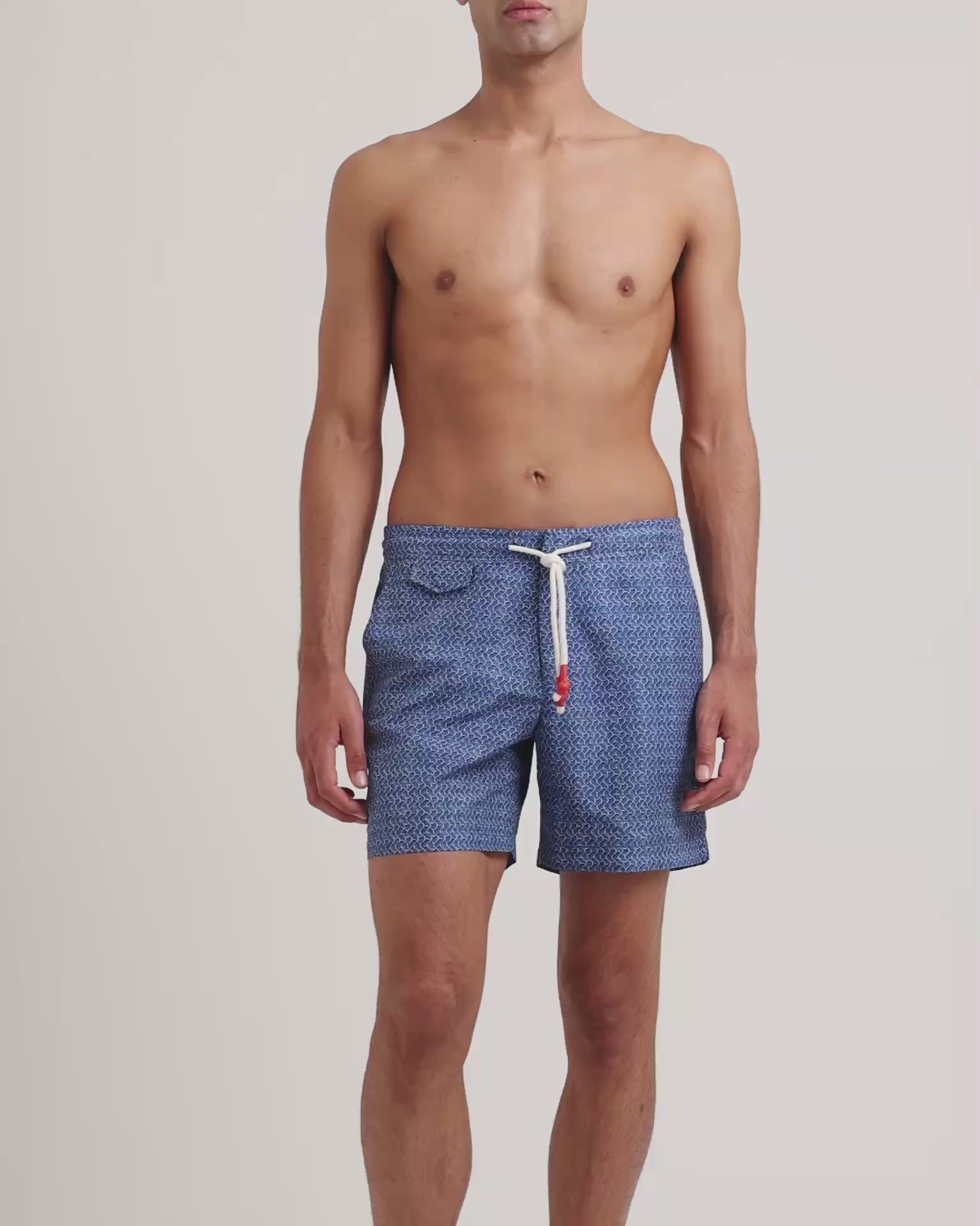 Man wearing geometric print blue drawstring swim shorts on a plain background