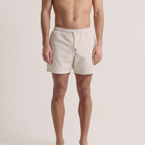 Man wearing beige seersucker swim shorts on a plain background