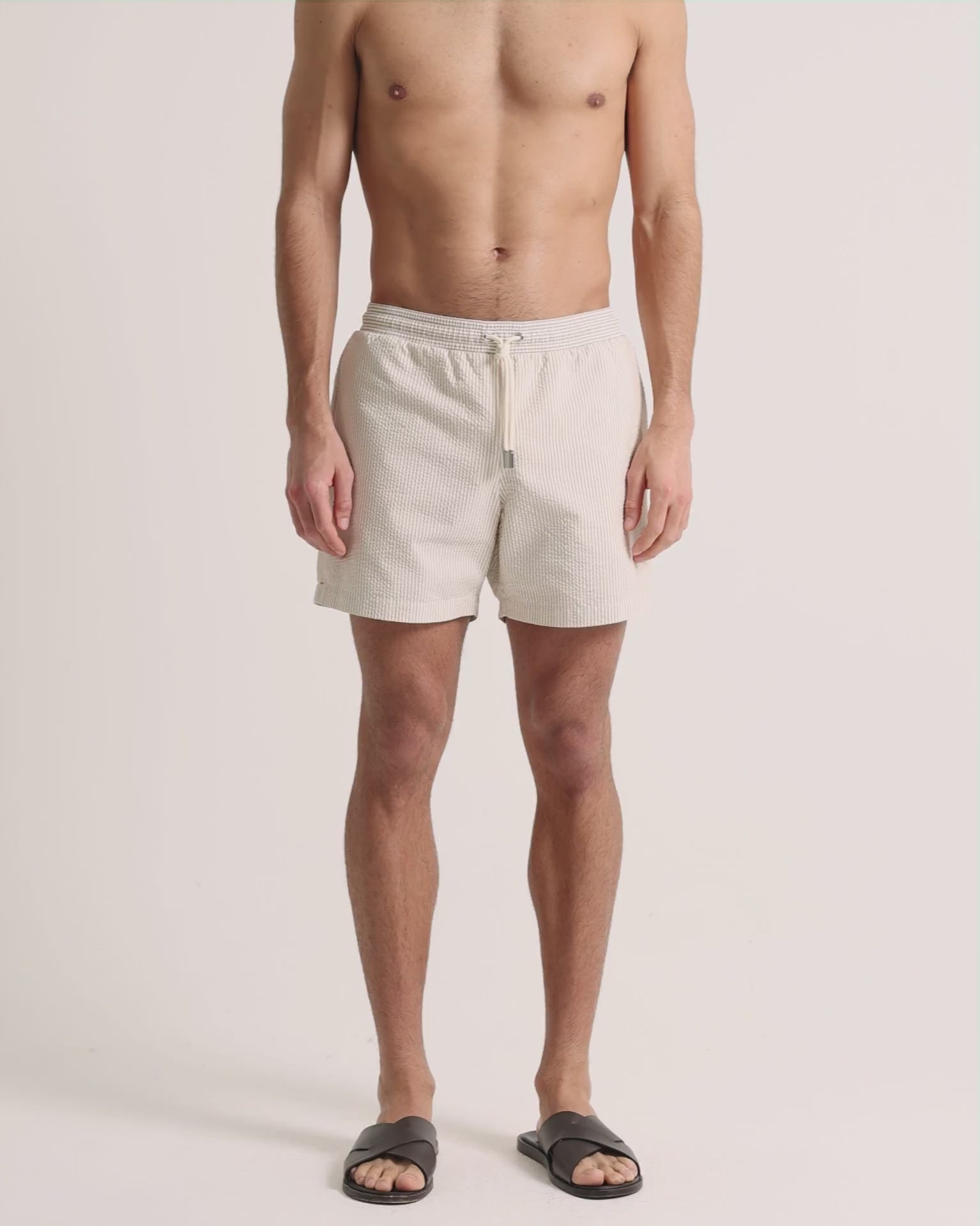 Man wearing beige seersucker swim shorts on a plain background