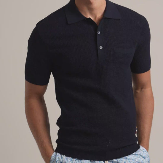 Man wearing navy mesh stitch polo shirt with chest pocket and blue patterned swim shorts against a plain background