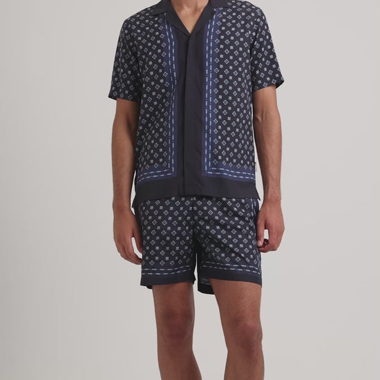 Man wearing a navy geometric print shirt with matching shorts on a plain background
