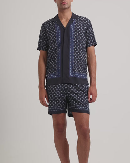 Man wearing a navy geometric print shirt with matching shorts on a plain background