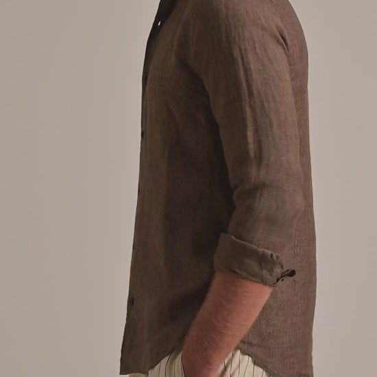 Man wearing brown linen shirt with light beige striped trousers on a plain background