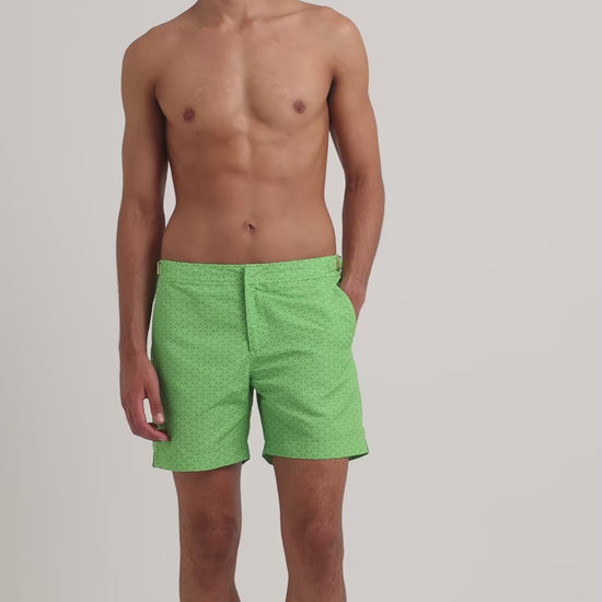 Man wearing green printed swim shorts on a plain background