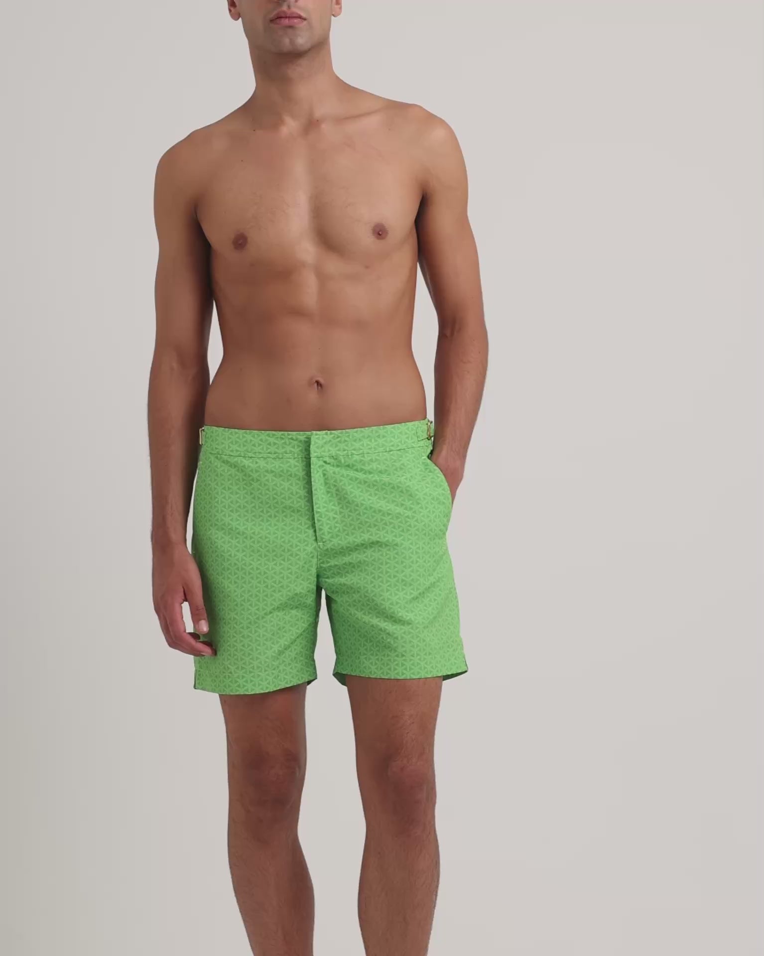 Man wearing green printed swim shorts on a plain background